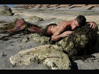 Merman laying on rocky beach strewn with seaweed